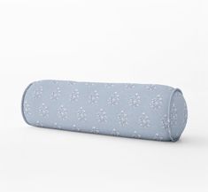 a rolled up blue and white pillow on top of a white surface with flowers all over it