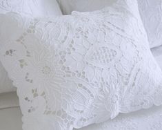 a white bed with two pillows on top of it and one pillow has an intricate lace design