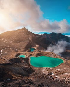 the blue lakes are surrounded by mountains and clouds in the sky, with steam rising from them