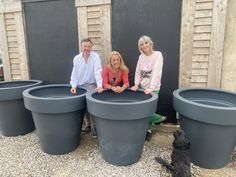 three people and a dog are sitting in front of large planters on the ground