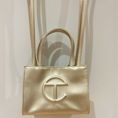 Authentic, Great Condition Small Gold Telfar Bag 100% Vegan Leather Sold Out On Telfar Website Authenticated By Fashionphile Party, Small, Going Out Bag Trendy Gold Color Iconic Unisex Shopping Everyday Bag Double Strap (Handle And Crossbody Strap) Embossed Logo Magnetic Snap Closure Materials: 50% Polyurethane, 50% Polyester Dimensions: Height 4 3/4", Width 6 5/8", Depth 3", Strap Drop 21", Handle Drop 4 3/4" Comment If You Have Any Questions! Luxury Gold Box Bag For Shopping, Designer Gold Bags With Double Handle, Designer Gold Double Handle Bag, Designer Gold Tote Box Bag, Designer Gold Bag With Detachable Handle, Tan Box Bag With Gold-tone Hardware For Shopping, Luxury Gold Tote Box Bag, Gold Box Bag With Handles For Travel, Double Handle Evening Bag With Dust Bag For Shopping