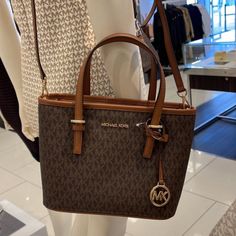 Michael Kors Jet Set Travel Xs Carryall Tote Top Zip Tote Brown Color: Brown Gold Toned Hardware Zip Top Closure Slip-In Pocket One Mk Charm Custom Fabric Lining 1 Slip-In Pocket, 1 Zipper Pocket 9"(Top) 11"(Bottom) X 7.75" (H) X 4.25"(D) Strap: 5", 24" Brown Tote Bag Outfit, Tote Bag Outfit, Michael Kors Clothes, Brown Tote Bag, Michael Kors Tote Bags, Carryall Tote, Travel Tote Bag, Blue Tote, Brown Tote