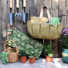 gardening tools and flowers are sitting on the ground next to a wooden fence with plants in it