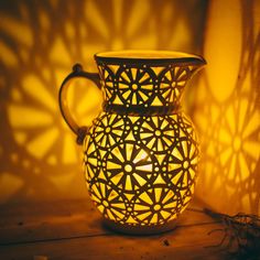 a white vase sitting on top of a wooden table next to a wall with shadows