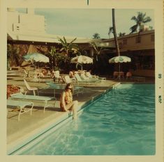 a woman sitting on the edge of a pool next to lounge chairs and umbrellas