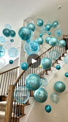 blue balloons are floating down the stairs in this home's entryway, which is decorated with glass balls