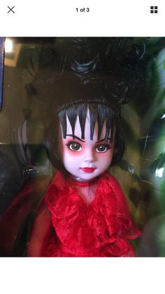 a doll with black hair and green eyes in a red dress sitting on top of a table