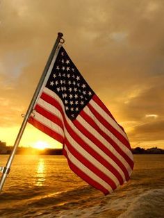 the american flag is waving in the wind on a boat at sunset or sunrise,