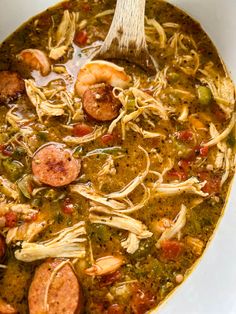 a white bowl filled with soup and sausages on top of a table next to a wooden spoon