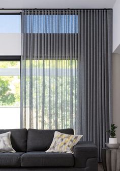 a living room with a gray couch and large window covered in sheer drapes on the windowsill