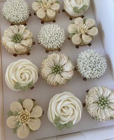 twelve cupcakes with white frosting and green flowers on top are in a box