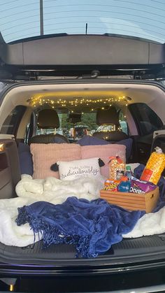 the back end of a car filled with blankets and pillows, food and drinks on it's trunk