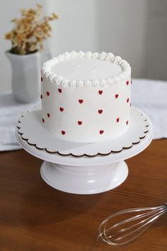 a white cake sitting on top of a wooden table next to a whisk