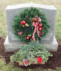 a wreath on top of a grave surrounded by evergreens and pomegranates