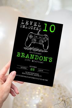 a hand holding up a black and green video game birthday party card that reads level unlocked 10 brandon's 20th birthday