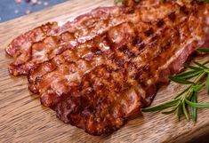 two pieces of meat sitting on top of a wooden cutting board next to green herbs