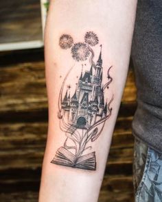 a person with a book and castle tattoo on their arm that has fireworks coming out of it