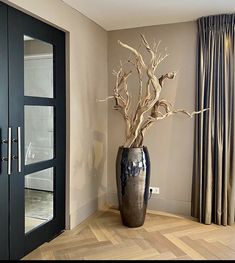 a vase with some branches in it sitting on the floor next to a door and window