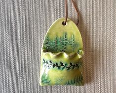 a ceramic ornament hanging from a cord on a carpeted surface with trees in the background