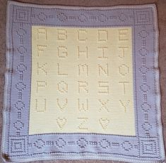 a crocheted blanket with the letters and numbers on it, sitting on carpet