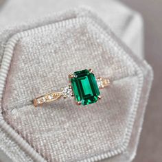 an emerald and diamond ring sitting on top of a white cloth