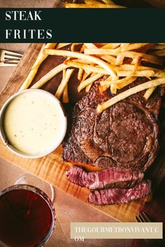 steak and french fries on a cutting board with sauce in a glass next to it