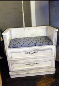 a white dresser with a gray cushion sitting on it's top shelf and bottom drawer