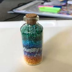 a glass bottle filled with lots of different colored pebbles on top of a white table