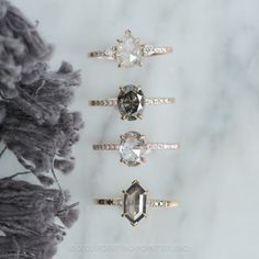 three different types of engagement rings on a marble surface with feathers in the foreground