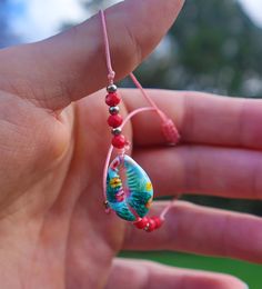 a person holding a beaded necklace in their hand with beads on the end and an object hanging from it's string