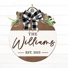 the williamss sign hanging on a white wooden wall with green leaves and ribbon around it