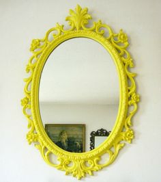 a yellow mirror sitting on top of a white wall next to a dresser and painting