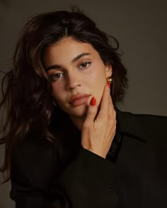 a woman with her hand on her chin, wearing a black jacket and red nail polish