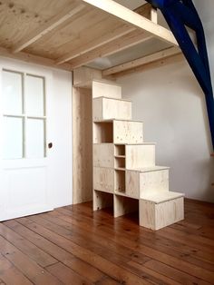 a room with wooden floors and stairs in the center, next to a white door