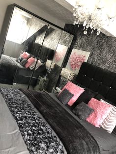 a bedroom with black and pink decor, chandelier and mirrored wall panels on the headboard