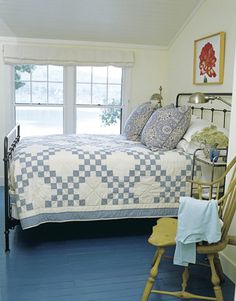 a bed room with a neatly made bed next to a chair and a large window