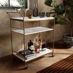 a bar cart with liquor bottles and glasses on it next to a potted plant