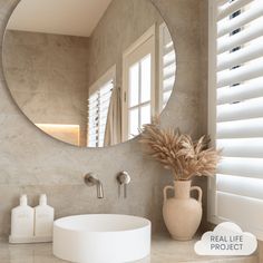 a bathroom with a round mirror above the sink and a white vase on the counter