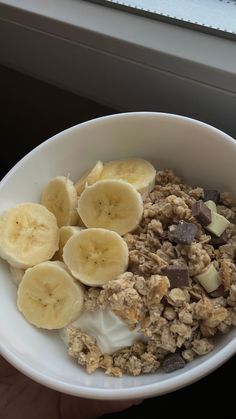 a bowl filled with cereal and bananas on top of a table next to a window