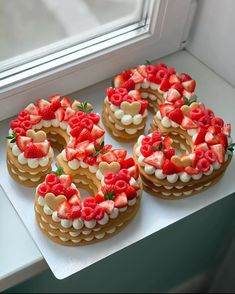 four cakes decorated with strawberries and cream on a window sill next to a window