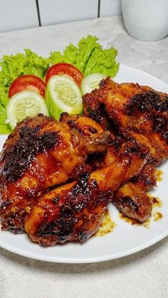 two chicken wings on a white plate with lettuce and tomatoes