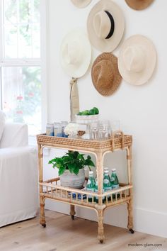 hats are hanging on the wall above a wicker cart with bottles and glasses in front of it