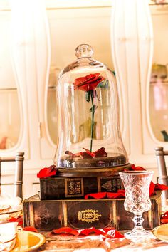 a glass bell jar with a rose in it sitting on top of a table next to plates and glasses