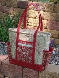 a red and white tote bag sitting on top of a brick wall next to flowers