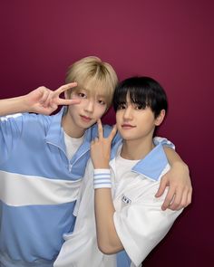 two young men posing for the camera in front of a purple wall with their fingers up