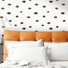 a bed with white sheets and pillows in front of a wall with black eyes on it