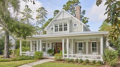 a white house with porches and chairs on the front lawn, surrounded by trees