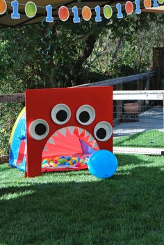 a red monster tent with eyes and mouth on the grass next to a blue ball