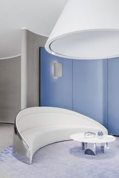 a curved white couch sitting in front of a blue wall with a lamp above it