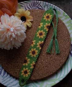 a piece of beaded art on a plate with flowers in the middle and an orange flower next to it